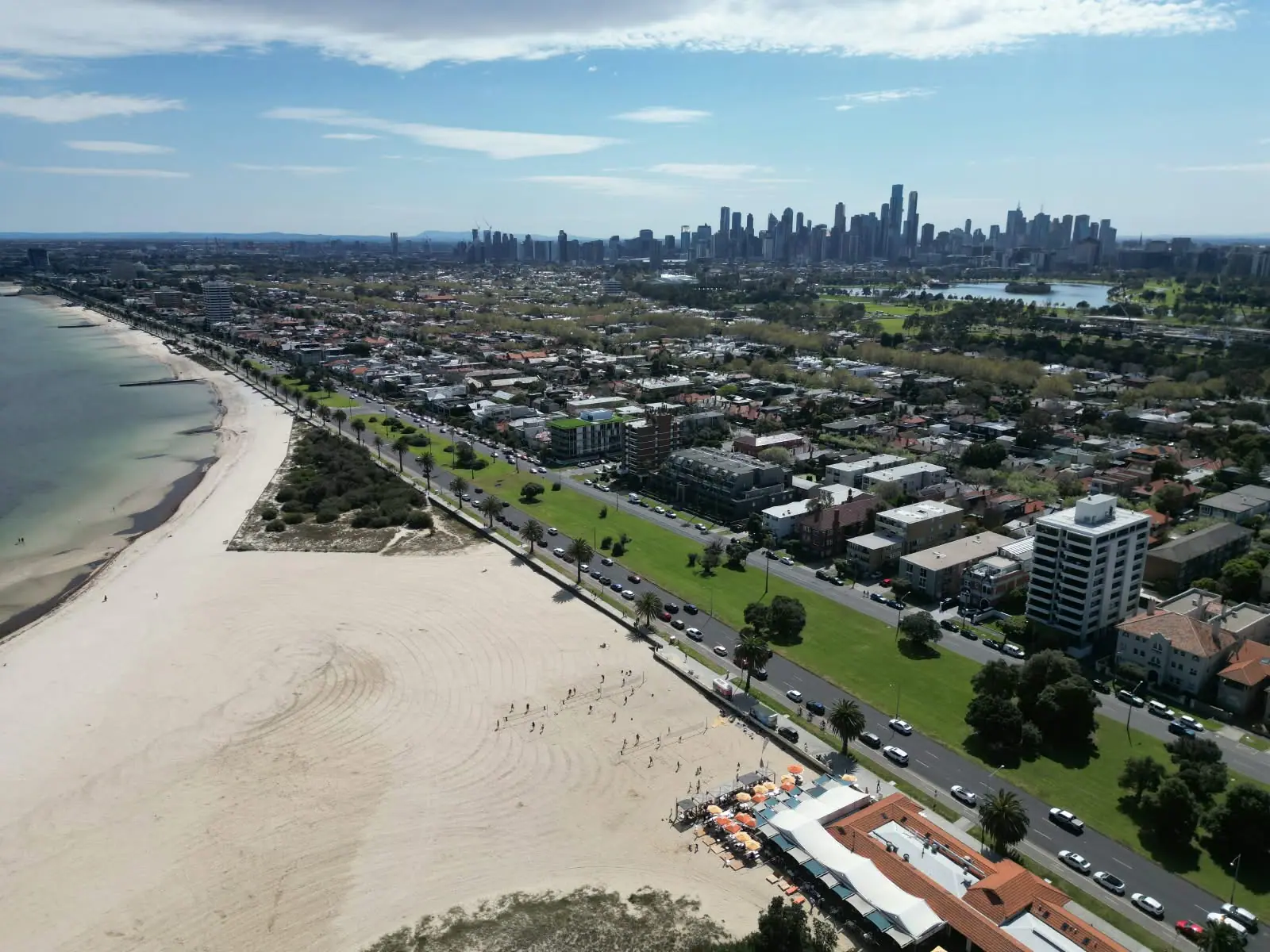 St Kilda beach from the air, with the courts and the West Beach Pavilion in the foreground and the Melbourne skyline behind