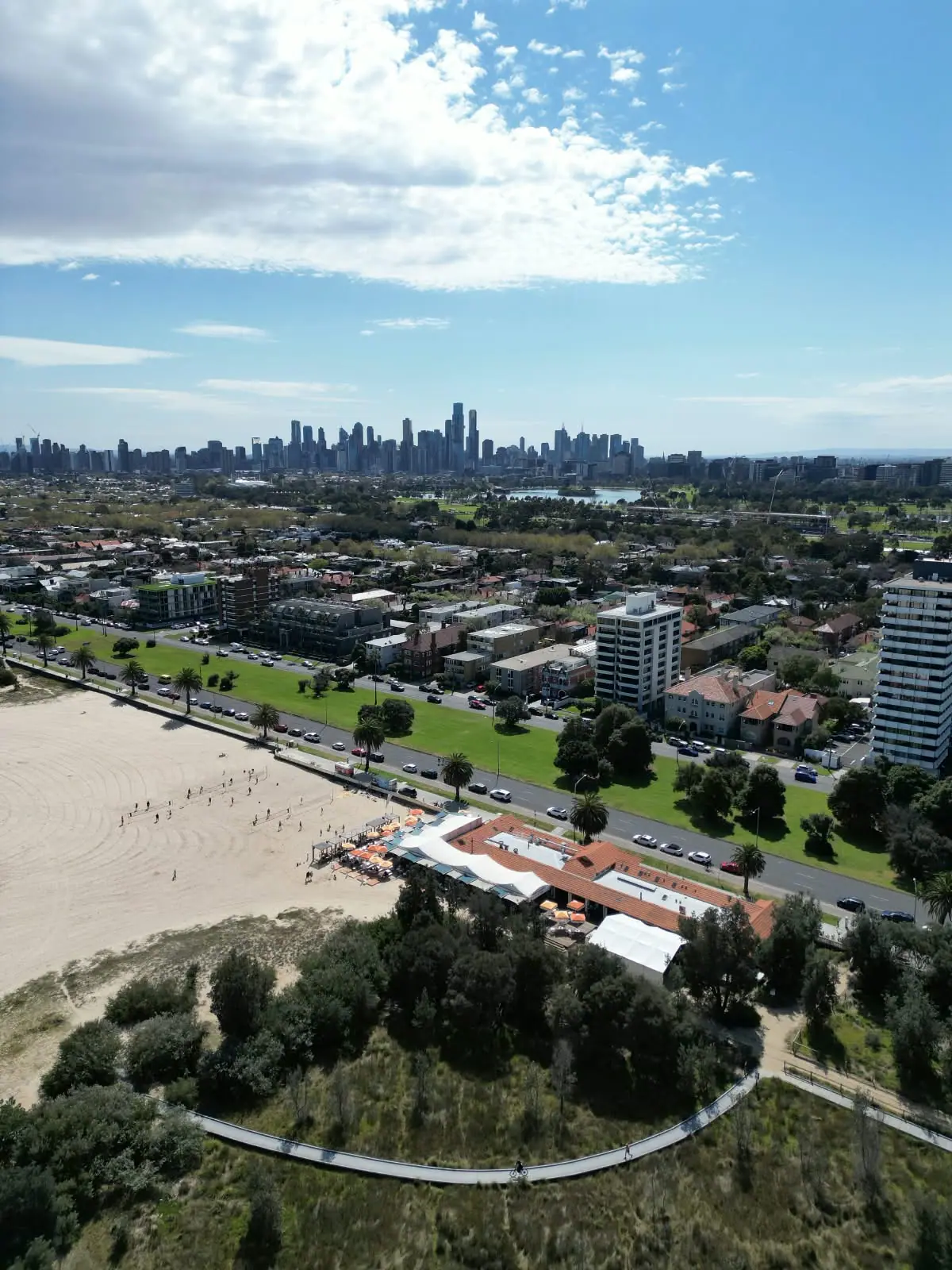 St Kilda beach from above, with the courts in play and the West Beach Pavilion below the Melbourne skyline